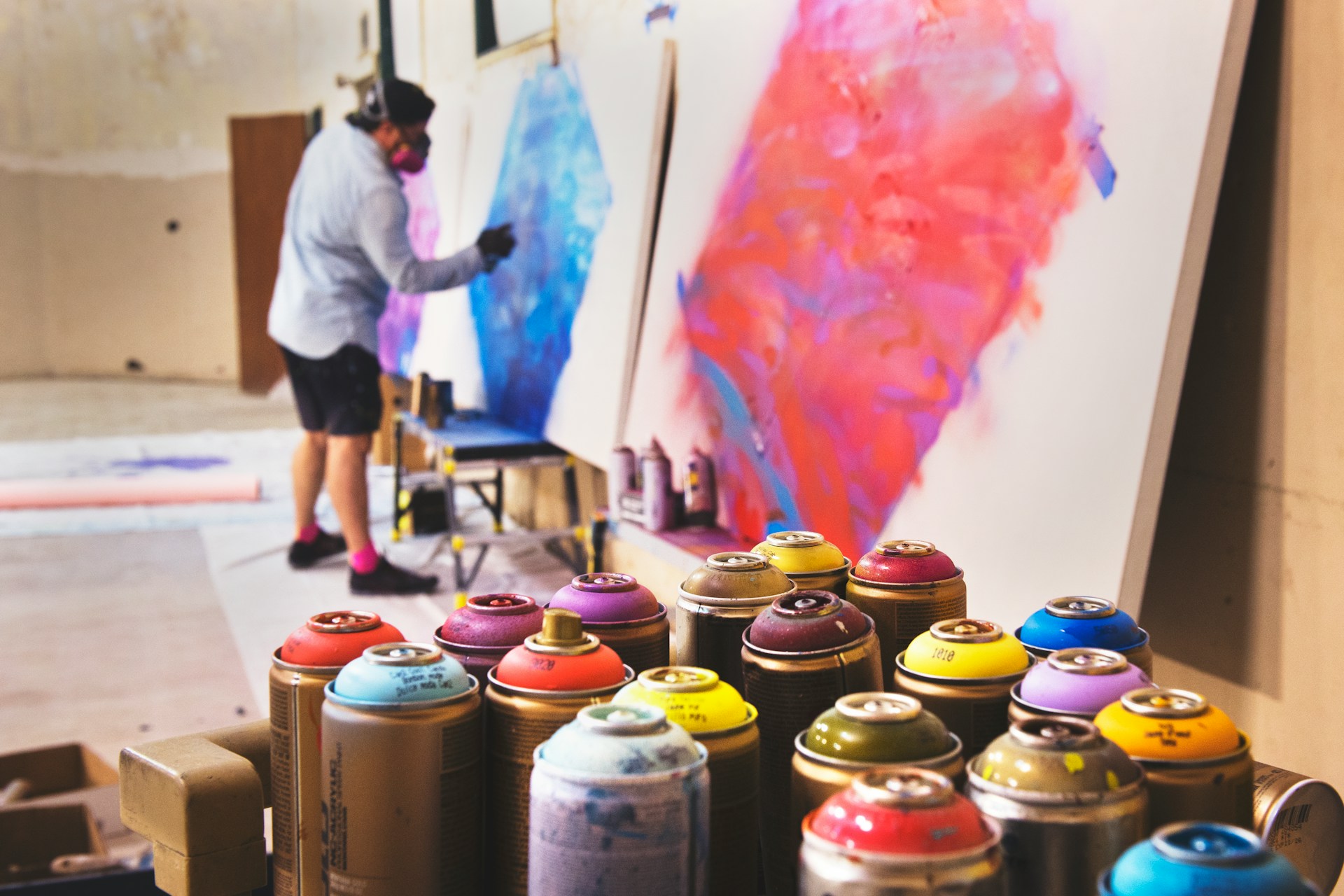 Spraypaint cans on a table with graffiti artist working in the background